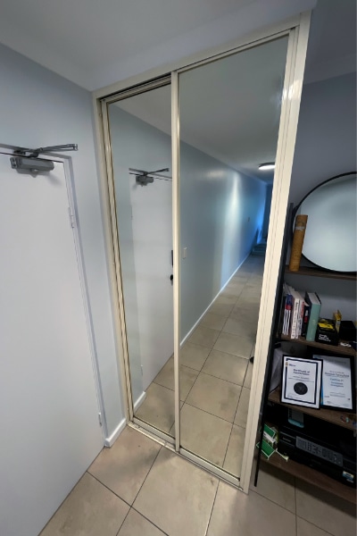 Small room featuring a narrow sliding mirror cupboard with dated cream frames and tracks