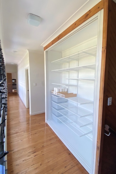 Renovated hallway linen cupboard with doors removed, revealing a newly lined back wall, sides, and the installation of Elfa shelving systems.