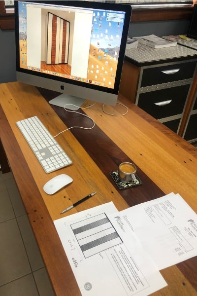 Carl's desk, featuring a paper quote and a computer screen showcasing a photo of a beautifully completed wardrobe installation, highlighting our dedication to quality and attention to detail.