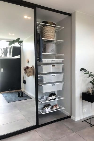 Budget-friendly mirror sliding doors in black frames, partially open to reveal a custom Elfa shelving storage system inside a modern wardrobe.