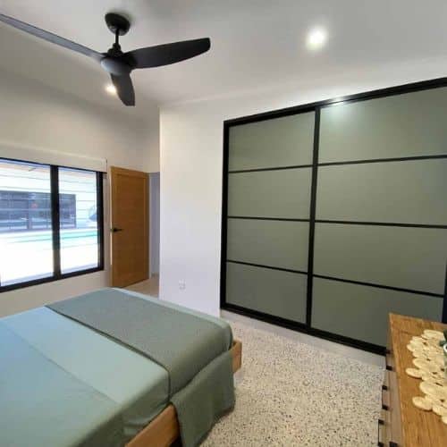 Bedroom with matt olive green sliding wardrobe doors framed in black, matching the room's minimalist decor.