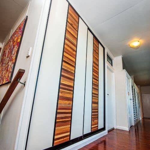 White sliding wardrobe doors featuring vertical strips of woven pine timber matching the timber floor.